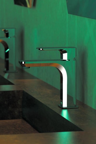 Een kraan afbeelding van twee Tiara chrome moderne wastafelkranen op een bruin granieten wastafelblad gemonteerd tegen een groene muur in een zeer moderne badkamer.
